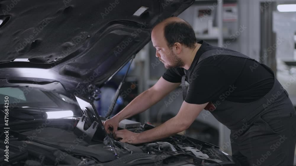 Mechanic Using A Digital Tablet to search for approval and diagnose car breakdowns. use of technologies for repair of vehicle. Auto service and maintenance of trucks. Car mechanic fixing Mechanic Using A Digital Tablet to search for approval and diagnose car breakdowns. use of technologies for repair of vehicle. Auto service and maintenance of trucks. Car mechanic fixing