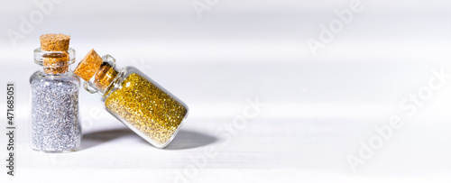 Small Glass jars with golden and silver glitters for nail art and makeup on white background, Copyspace, Banner