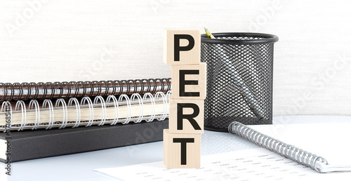 PERT text on the wooden block with notebooks on the chart