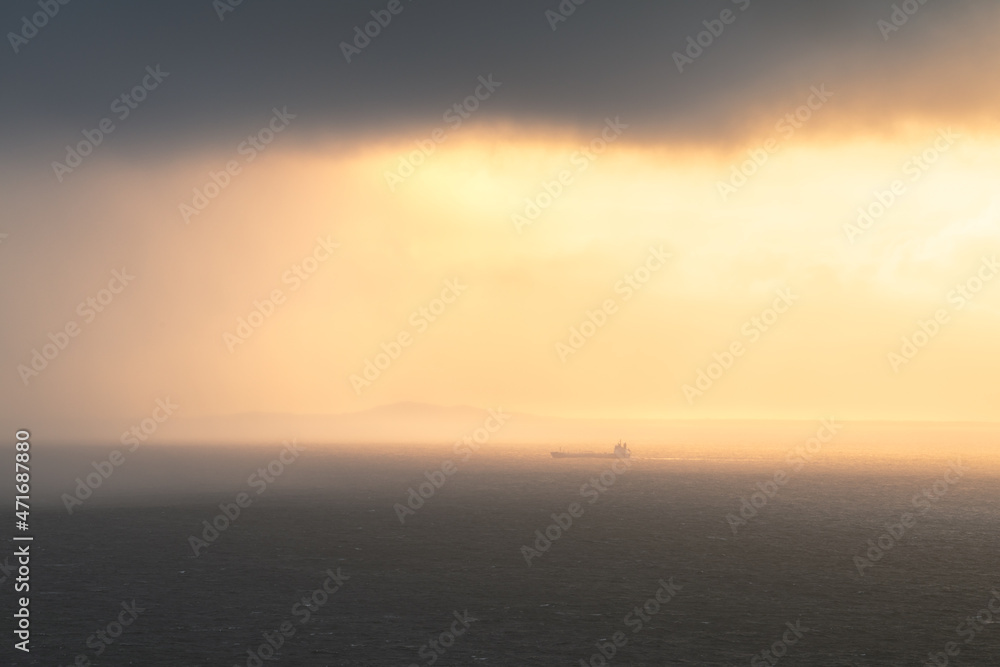 Large ferry boat at sea in far distance with beautiful sunset light filtering through clouds. Scottish Hebrides, United Kingdom. Travel and transportation backgrounds.