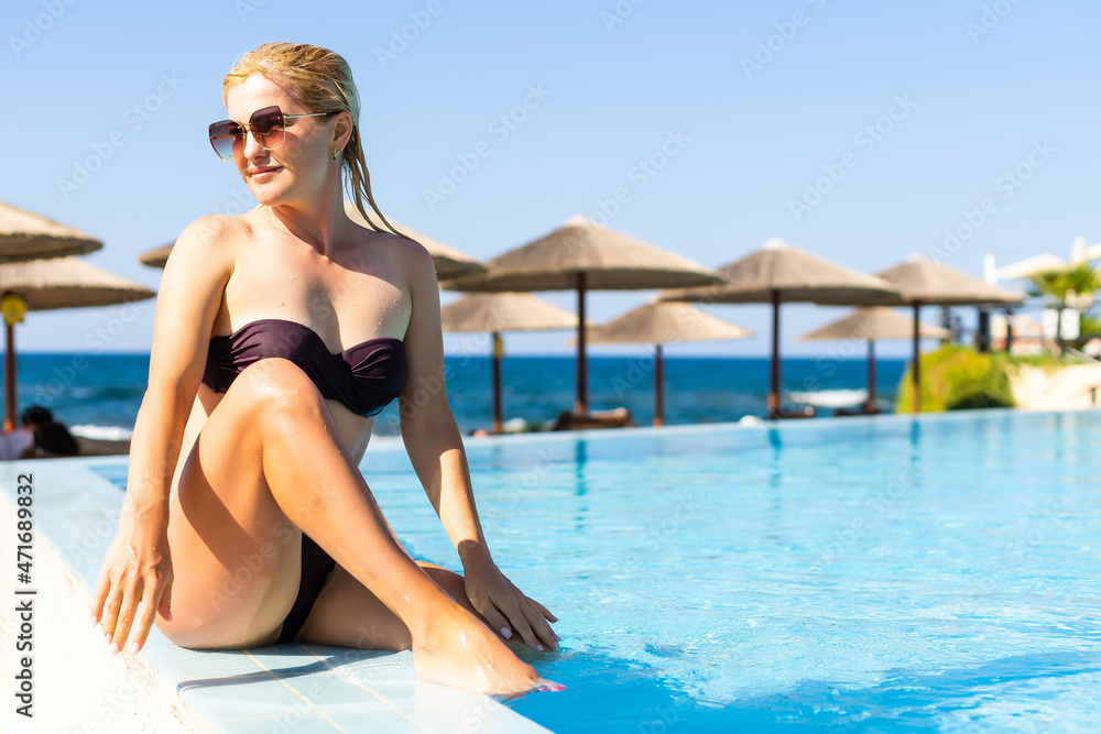 Young woman relaxing in swimming pool on summer vacation. Blonde, caucasian.