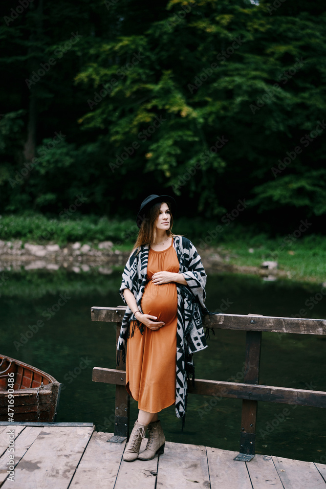 Pregnant woman leans on the railing of the pier with boats on the lake