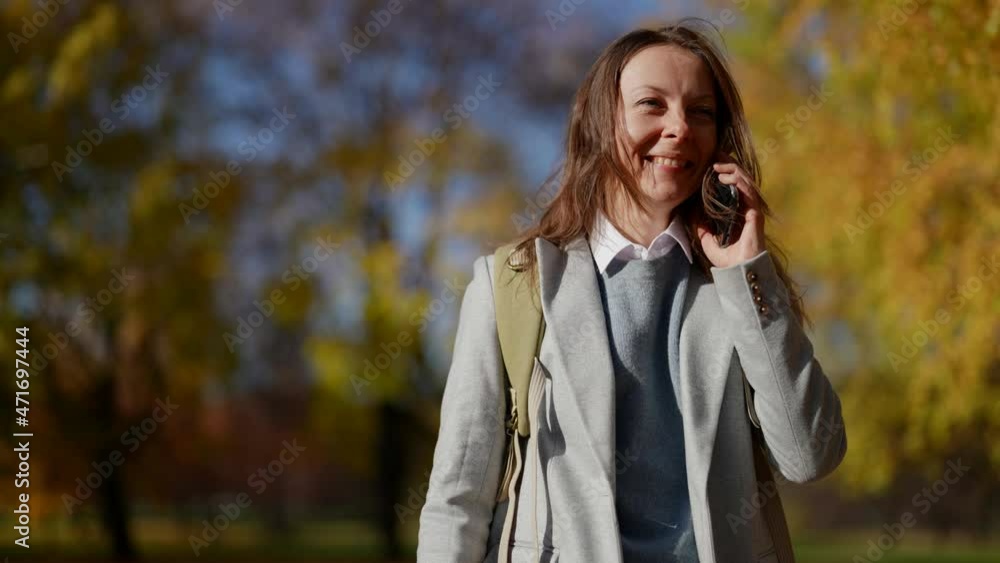 An attractive adult happy woman dressed in casual clothes and using a smartphone in a city park. Communicating with people online conversation on the street in autumn An attractive adult happy woman dressed in casual clothes and using a smartphone in a city park. Communicating with people online conversation on the street in autumn