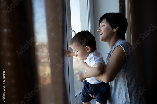 little boy with his young beautiful mother look out the window