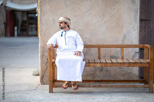 Photography Arab Man in Al Seef district in dubai seating outside his shop and enjoying the