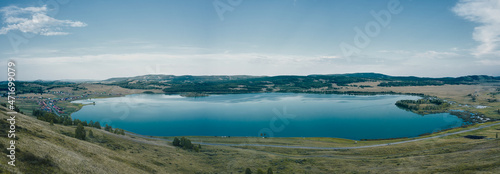 Blue surface of lake, Turquoise water lake, countryside landscape in summer sunny day, sky reflected on water surface, rural terrain with field, hills and mountains, Bashkortostan republic in Russia