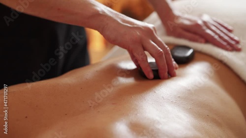 Hot stones massage. Close-up of masseuse placing hot stones on young man's back photo