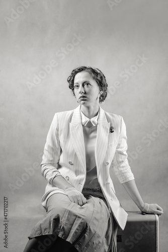 Young woman dressed in retro style sitting on a suitcase. Studio shot