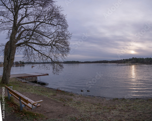 Pale Winter solstice reflex in the calm lake M  laren  jetty and an empty bench in the district Bromma in Stockholm