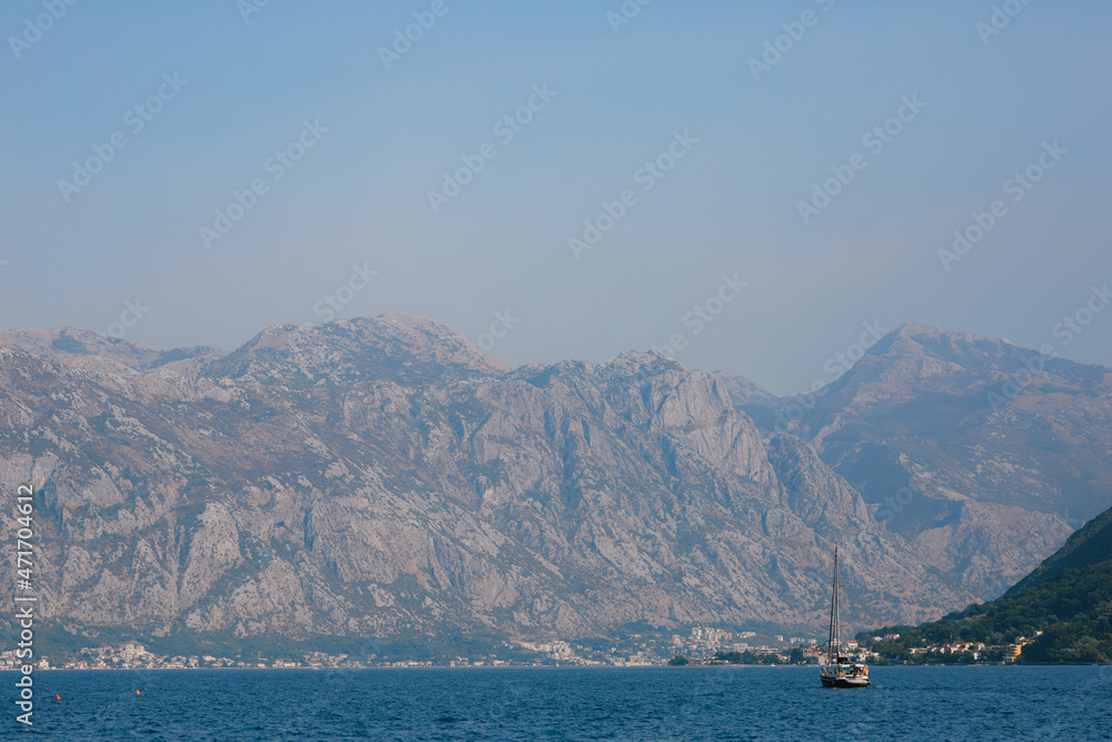 Sailboat floats to the mountains in the haze along the Kotor Bay. View from Perast. Montenegro