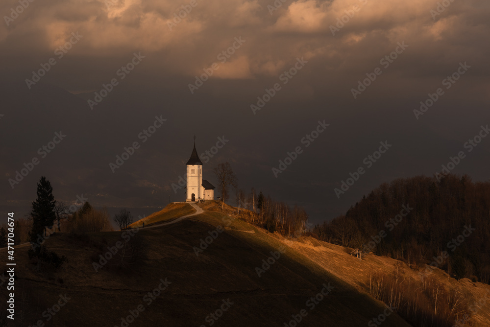 Incredible views of the famous landmark. Artistically painting sunlight highlights the beauty of the chapel. Evening. Church of Saints Primozh and Felitsian. The village of Yamnik. Slovenia.