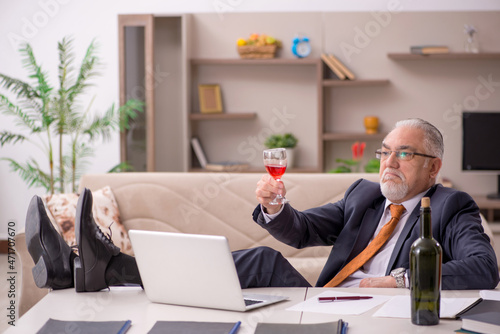Old male employee drinking champagne at home