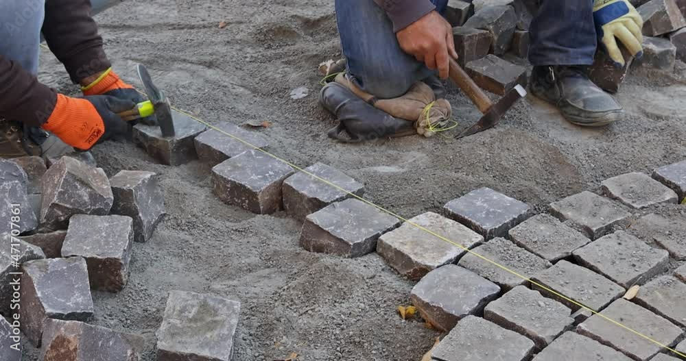 Industrial worker working paving using hammer pavement with granite stones cobblestones for paving road Industrial worker working paving using hammer pavement with granite stones cobblestones for paving road
