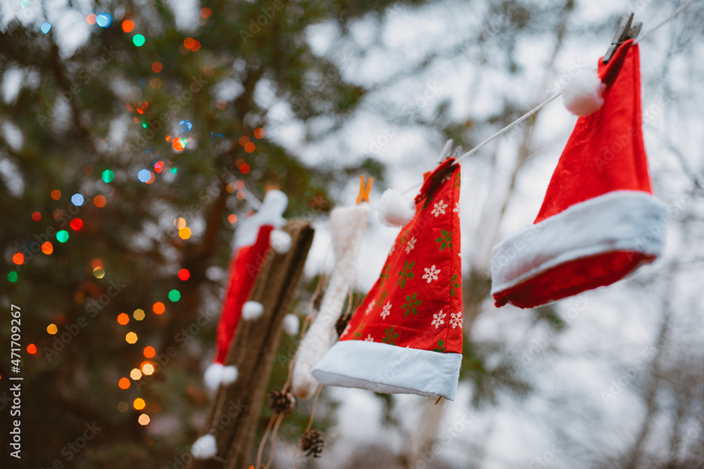 Santa Claus hats hang on a clothesline in the forest against
