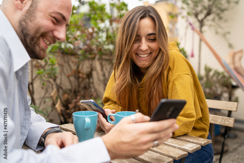 Happy couple enjoying media content in a smart phone sitting on a cafe table drinking coffee. Happy couple enjoying media content in a smart phone sitting on a cafe table drinking coffee.