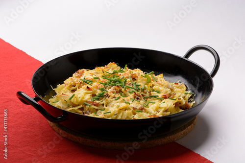 Traditional Austrian Dish so called Schinkenfleckerl in ablack pan with red and white background
