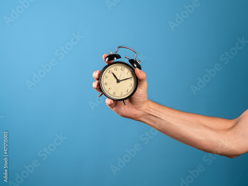 Wake up and get up, it's time to act, concept. Clock and alarm clock, attention it's time to do. A man's hand holds a vintage alarm clock, a photo on a blue background