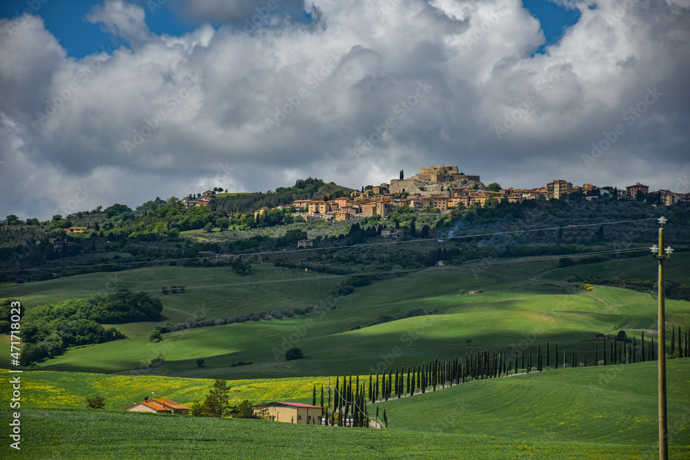 Tuscany, italy, may 2018, in the foreground a farm with a cypress alley, an old town in the distance on top of a green hill