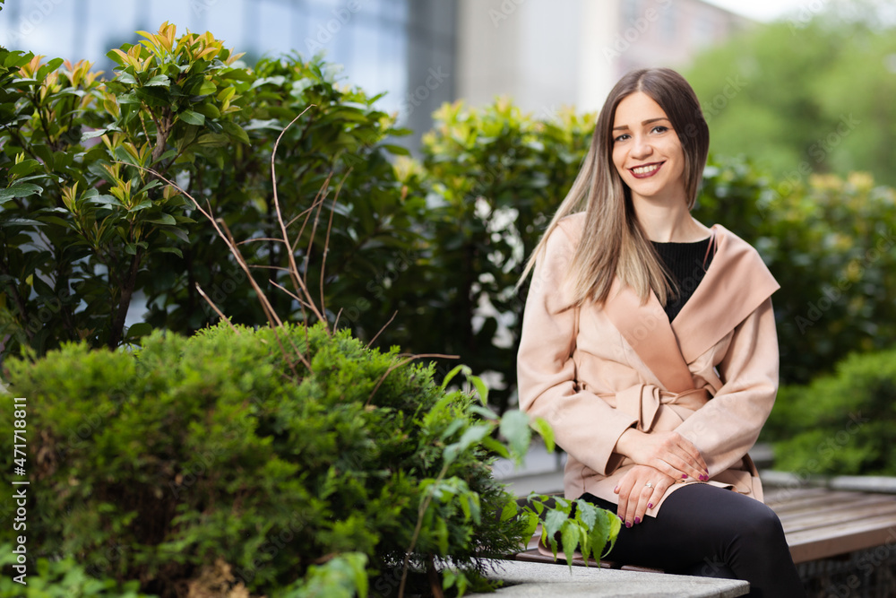Portrait of a woman sitting on a bench. Successful businesswoman posing outdoors surrounded by green plants. Portrait of a woman sitting on a bench. Successful businesswoman posing outdoors surrounded by green plants.