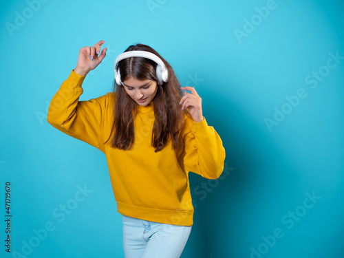 Music lover, a young woman with headphones, listening to music. A young brunette in a bright yellow hoodie uses wireless headphones for a smartphone.