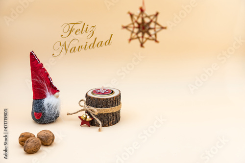 Postal navideña con texto en español Feliz Navidad y fondo beige, nueces, vela de madera y un gracioso gnomo photo