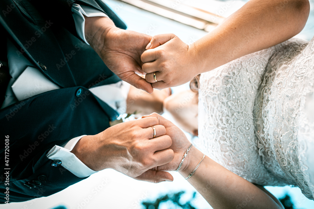 Fototapeta premium Joined hands of newlyweds capturing wedding rings. A kiss can be seen in the background. The hands of the newlyweds on which the wedding rings can be seen