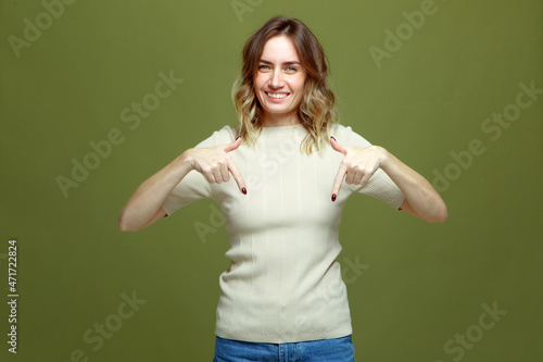 Happy young woman pointing fingers below indicating sale offer, smiling girl advertising, point down on green background