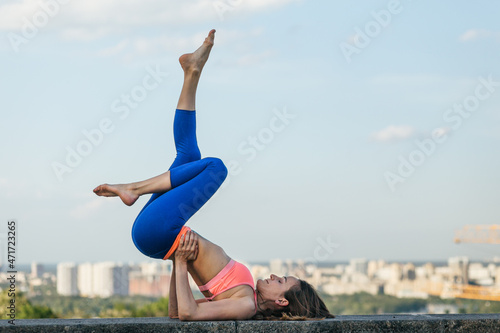Beautiful girl in sportswear doing yoga on a high parapet and a beautiful back view of the city, meditation and relaxation