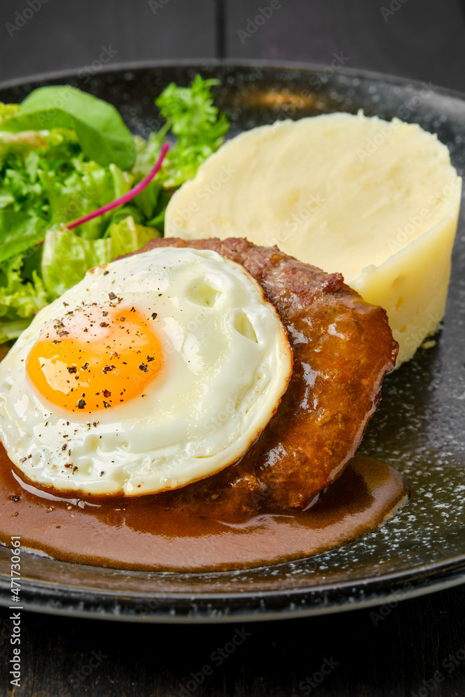 Closeup view of beef cutlet with fried egg, mashed potato and fresh salad Closeup view of beef cutlet with fried egg, mashed potato and fresh salad