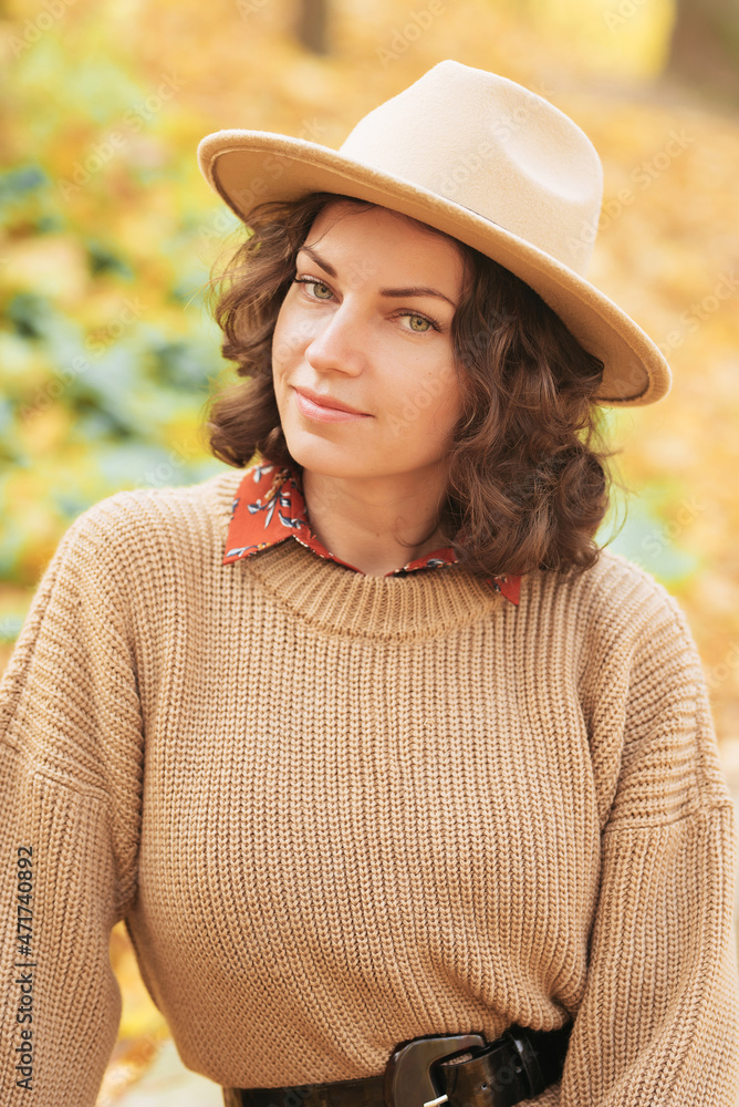 Portrait of a young beautiful and curly girl in an autumn park wearing a hat