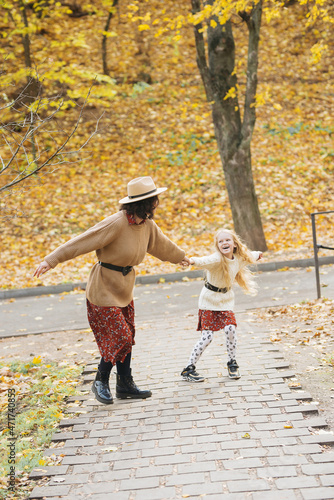 Mom and daughter are walking in beautiful colored dresses family look in an autumn park with leaves © mihalovna88