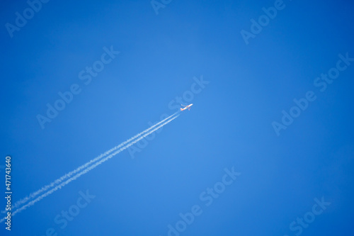 looking up at an Easyjet Airbus A320 twin engine jet airliner in deep blue sky with vapour trails diagonally across the frame