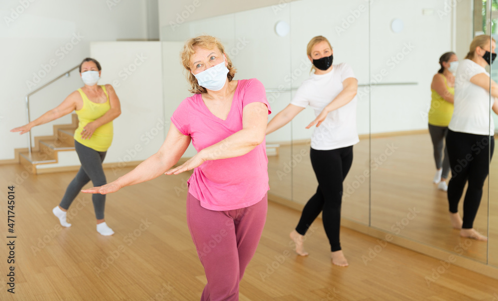 Three mature European women in masks are dancing in fitness room
