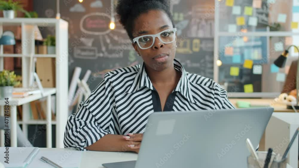 Slow motion portrait of young African American woman sitting in office and looking at camera with serious face. Business and people concept. Slow motion portrait of young African American woman sitting in office and looking at camera with serious face. Business and people concept.