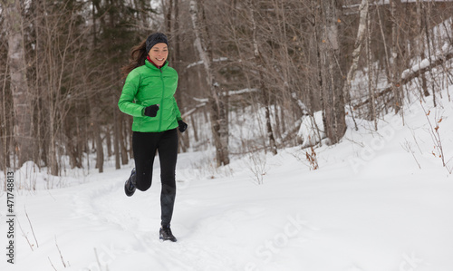 Running in Winter snow. Woman runner jogging outside on cold winter day in forest. Fit healthy lifestyle concept with beautiful young fitness model. Mixed race Asian Caucasian jogging in full length.