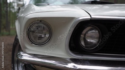 Old vintage car. White convertible cabriolet vehicle at the evening at country road. Muscle American auto front bumper, headlight and grill.