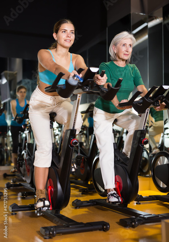 Young and adult confident women warming up on bikes in spinning class at gym