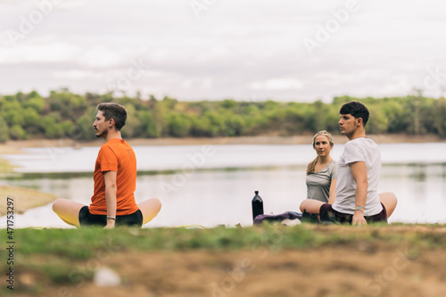 People stretching while doing yoga in a park next to a lake
