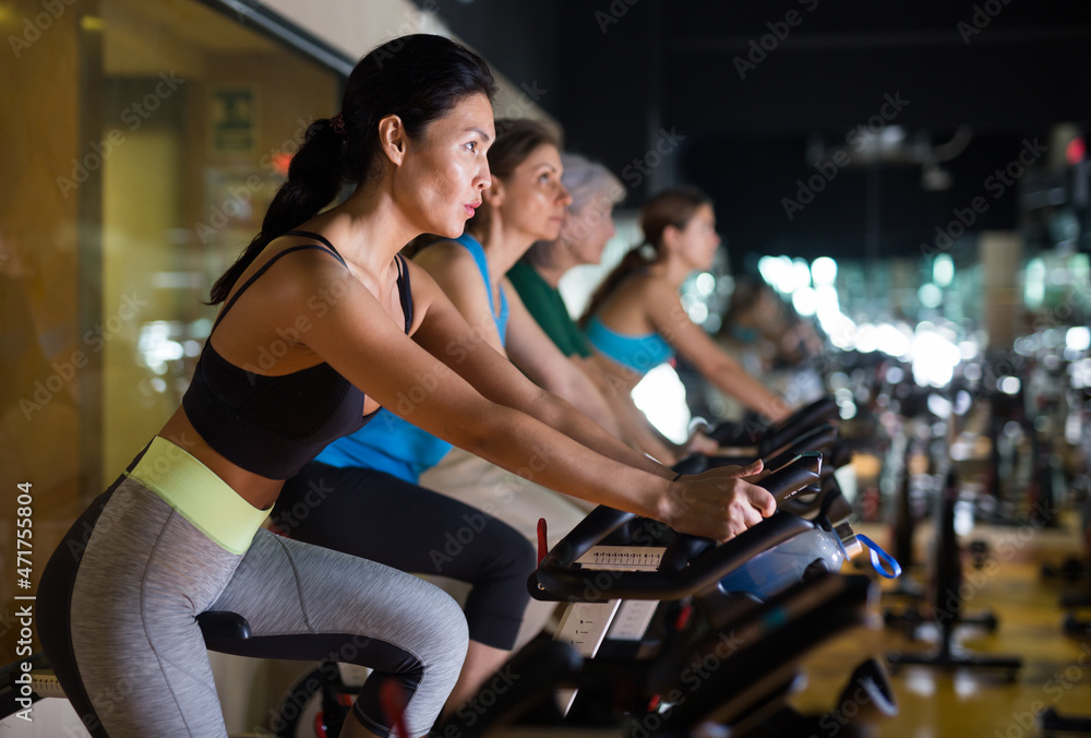 Fototapeta premium Asian woman in sportive activewear training on bike in spin class at gym