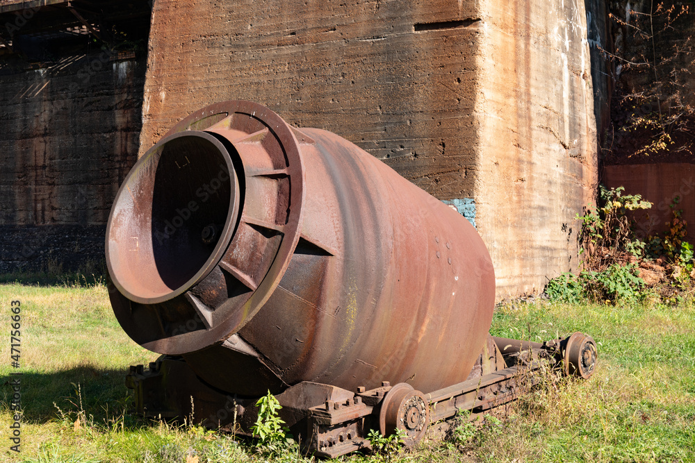 Rusting huge metal crucible on a wagon in a field of grass beside large concrete structures, horizontal aspect Rusting huge metal crucible on a wagon in a field of grass beside large concrete structures, horizontal aspect