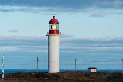 The watch room of a lighthouse.The lantern room has a large green bulb. The building is white with a red rail around the gallery deck.The background is cloudy and there s vignetting around the edges. 