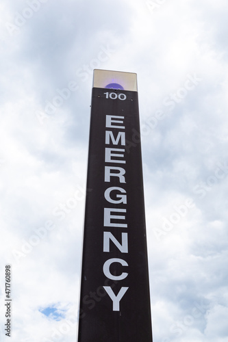 View looking up at a blue light emergency call box against a cloudy sky, vertical aspect