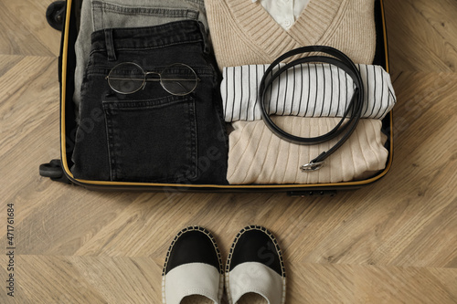 Open suitcase with folded clothes, accessories and shoes on floor, flat lay