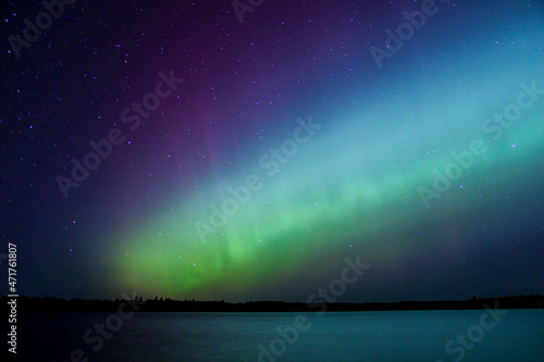 Northern lights erupt over Minnesota lake in the dark sky overhead shining a rainbow of Aurora light and colors over the forests and water photo