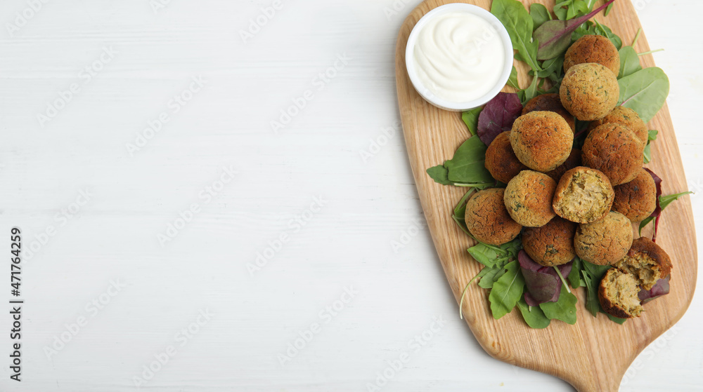 Delicious falafel balls with herbs and sauce on white wooden table, top view. Space for text Delicious falafel balls with herbs and sauce on white wooden table, top view. Space for text