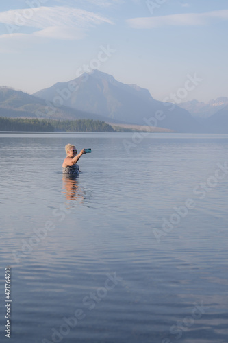 Blonde adult woman enjoys taking a dip in the cold waters of Lake McDonald in Glacier National Park and takes a selfie