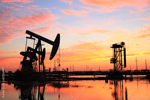 Photos in the evening, oil pumps are running, The oil pump and the beautiful sunset reflected in the water, the silhouette of the beam pumping unit in the evening