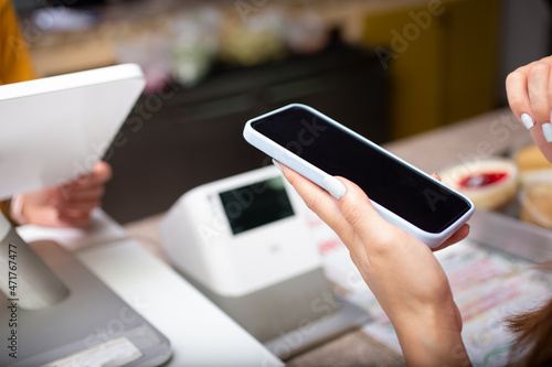A view of a person holding up a cell phone at the cash register of a retail store.
