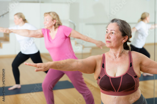 Elderly woman maintaining mental and physical health attending group yoga class at studio photo