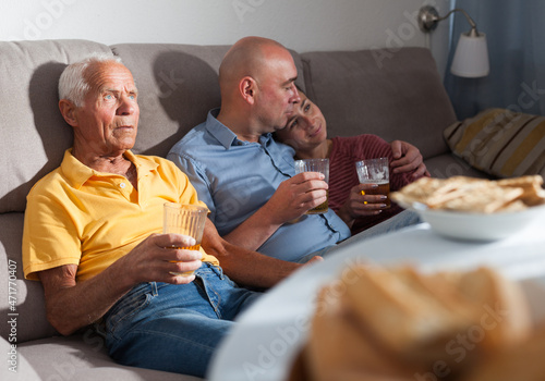 Family watching tv and drinking beer at home. High quality photo